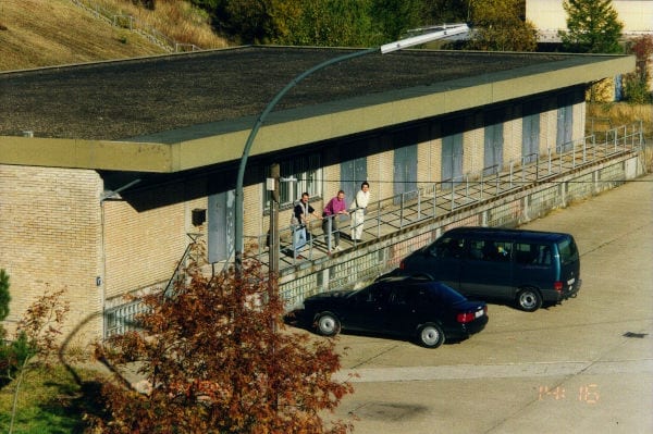 Drei Personen und Autos vor einem alten SincoTec-Gebäude.