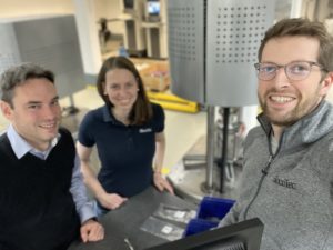 Drei Personen stehen vor einer Maschine im Prüflabor